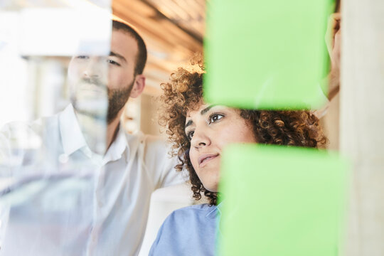 Two colleagues brainstorming with post-its on glass pane