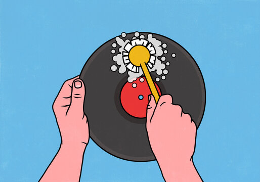 View from above of hands scrubbing a vinyl record with a dish brush against a blue background