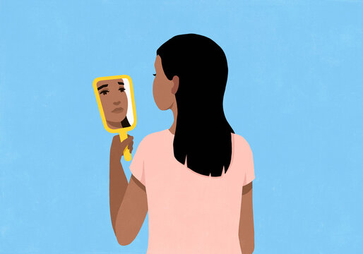 Sad, crying woman looking at reflection in handheld mirror against blue background