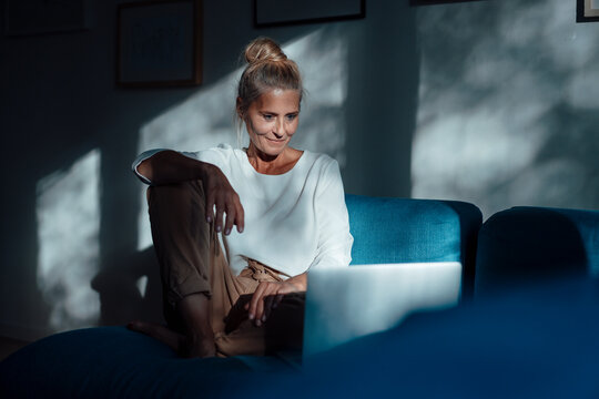 Woman with hand on knee using laptop at home