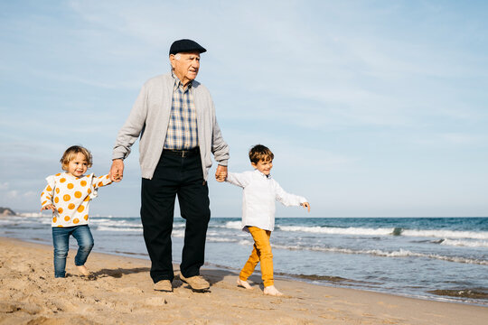 Grandfather strolling with his grandchildren hand in hand on the beach