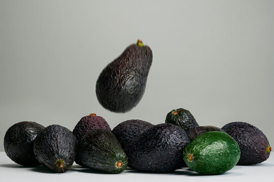 Blurred avocado falling toward group of avocados on gray background