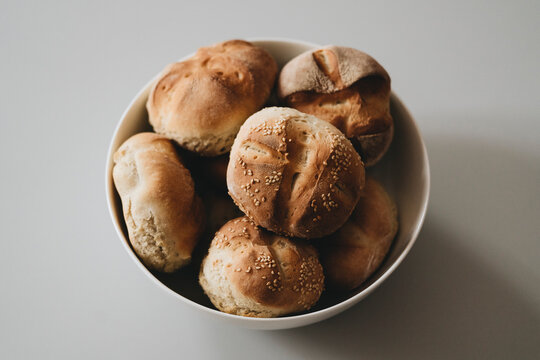 Close up still life of spelt rolls with seeded tops in round bowl against gray background
