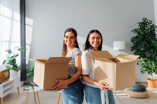 Smiling friends with cardboard boxes moving in new house