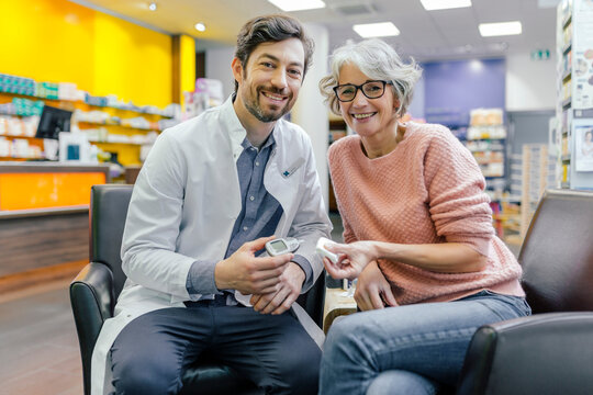 Portrait of smiling pharmacist and customer with blood sugar meter in pharmacy