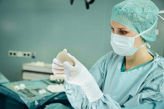 Female surgeon holding up and checking silicone implant during surgery