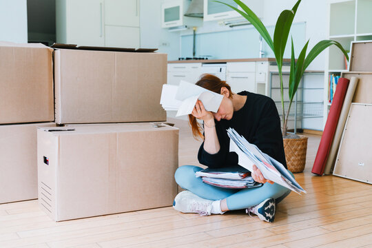 Upset woman sits on the floor with paperwork during moving day