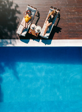 Two beautiful women sunbathing on a terrace next to the pool