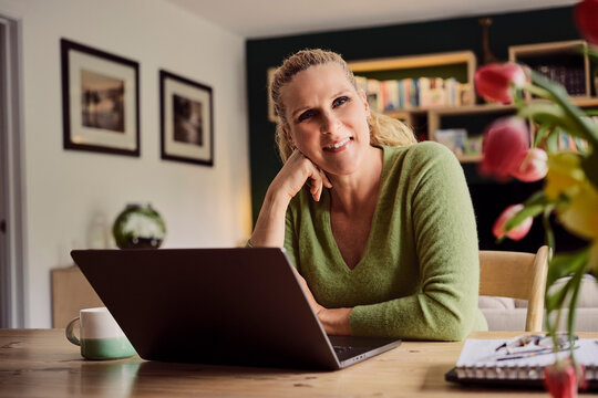 Happy woman uses a laptop computer for home working in the lounge