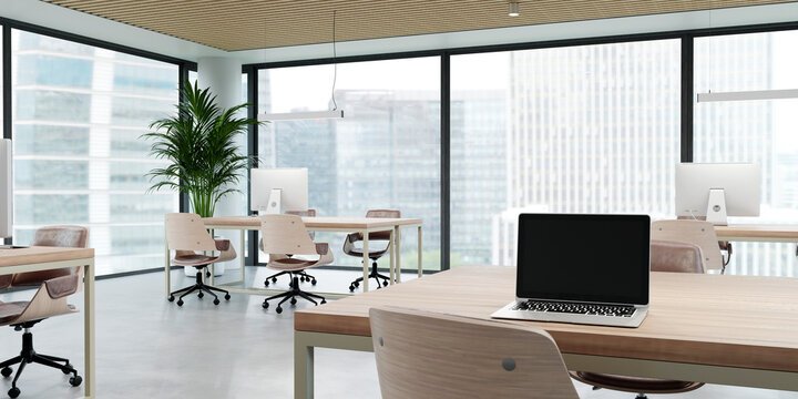 A modern open office interior features a desk and laptop