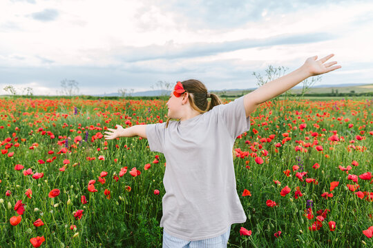 Girl enjoys freedom in a poppy field with outstretched arms