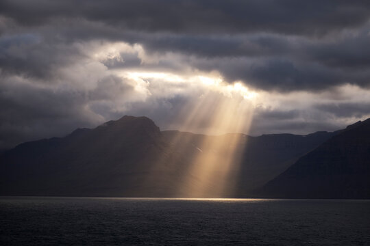 A bright sunbeam pierces a dark cloud over the ocean in Iceland