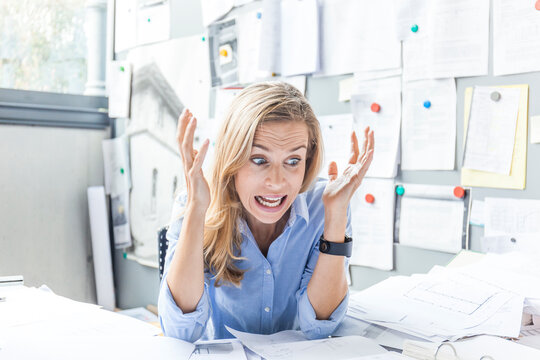 Angry woman sitting at desk in office surrounded by paperwork