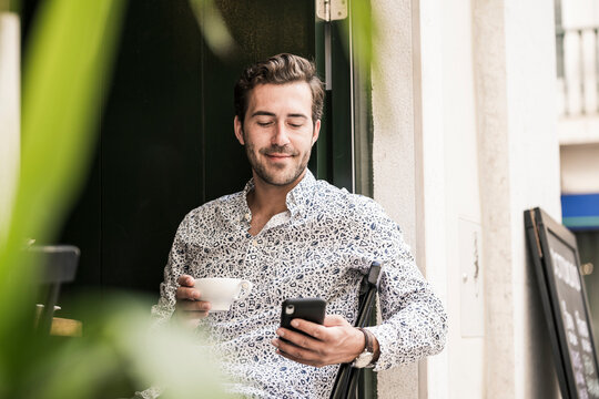 Young man with mobile phone having a coffee in a cafe in the city, Lisbon, Portugal