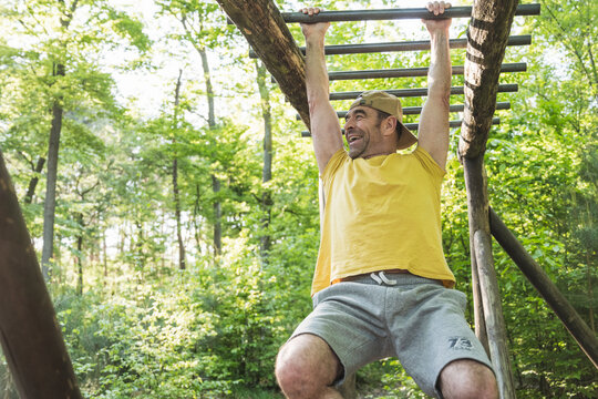 Low angle view of happy mature man hanging from monkey bars at park