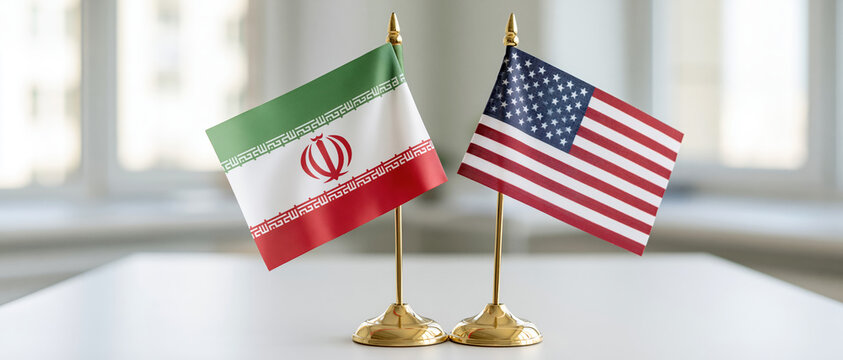 Two small desk flags of Iran and the United States on gold stands symbolize bilateral diplomacy, trade negotiation, or geopolitical tension. Ideal for news, editorial, and policy content.
