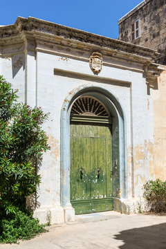 Elegant green wooden door framed by a weathered limestone facade in the historic fortified city of Mdina, Malta. Authentic Mediterranean architecture showcasing timeless heritage and classic design.