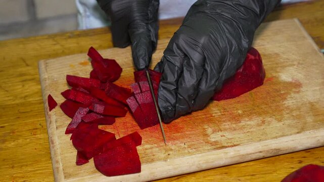 Chef chopping fresh beetroots on a wooden cutting board. High-angle close-up shot capturing precise culinary preparation of healthy organic red root vegetables.