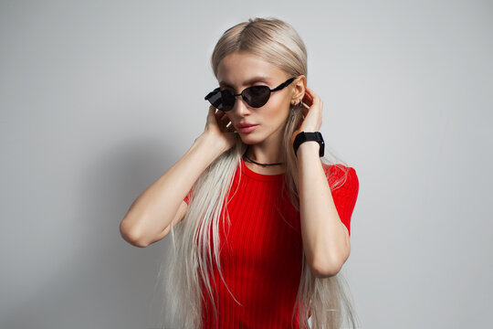 Young pretty blonde girl in red shirt wearing sunglasses isolated on grey background.