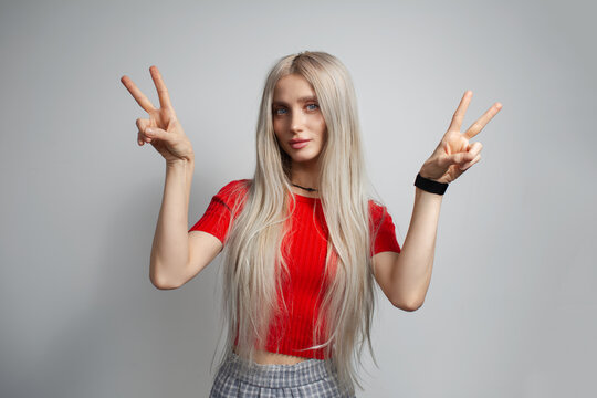 Young pretty blonde girl in red shirt showing peace gesture isolated on grey background.