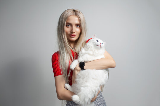 Young blonde girl with fluffy white cat in hands isolated on grey background.