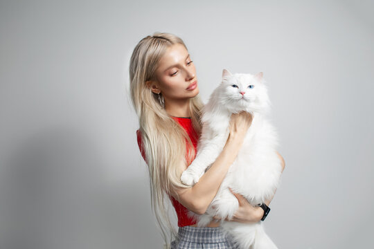 Young blonde girl with fluffy white cat in hands isolated on grey background.