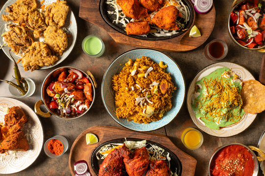 Overhead hero shot of an authentic Indian food spread featuring chicken biryani, tandoori chicken, chicken tikka, chicken pakora, chilli chicken, papdi chaat, curries, naan and traditional chutneys se