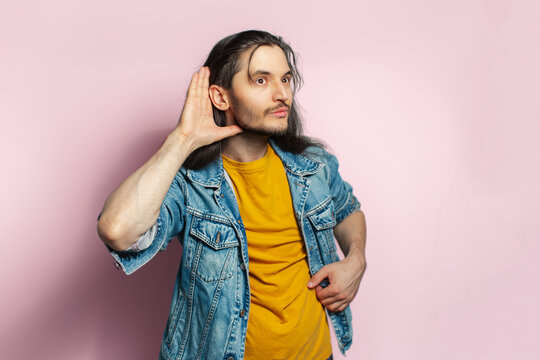 Young happy man with long hair. Doing gesture - I hear you. Isolated on pastel pink background.