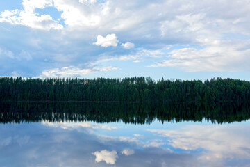 Fototapeta premium Beautiful sunny landscape by the lake in Finland. Clear water with blue and cloudy sky.