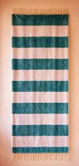 Obraz premium Textured green and cream striped woven fabric hanging with fringed edges on a plain background