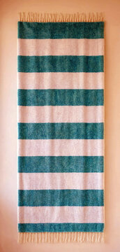 Textured green and cream striped woven fabric hanging with fringed edges on a plain background