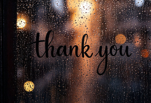 Thank you handwritten text on a raincovered window with warm bokeh lights shining through