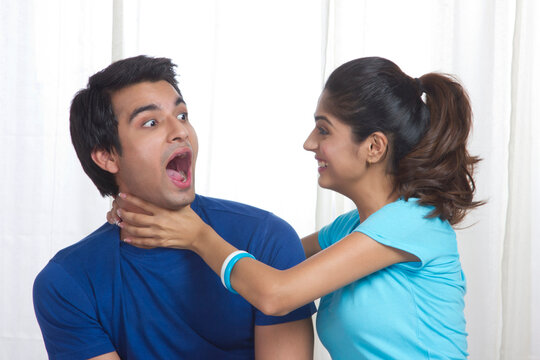 Playful young woman gripping man's neck at home