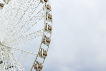 Giant white Ferris wheel structure with enclosed cabins against a cloudy sky © Artem Kniaz