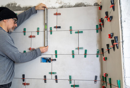 Experienced construction worker using a spirit level to ensure proper alignment and evenness when installing new ceramic tiles during a bathroom or kitchen renovation project