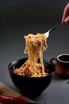 Hand twisting spaghetti bolognese with a fork over a black bowl on dark background. Action food shot.