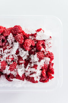 close up of frozen raspberries with ice crystals in clear container