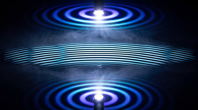 Mirrored beams of blue light rippling across a dark reflective surface