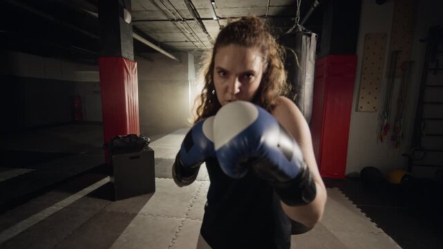 Portrait of young Caucasian woman raising boxing gloves into defensive stance in slow motion. Footage is ideal for female empowerment, mental resilience, and fitness marketing campaigns