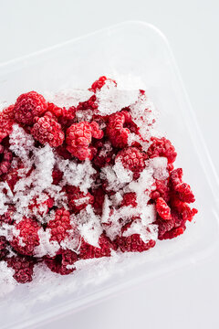 close up of frozen raspberries with ice crystals in clear container
