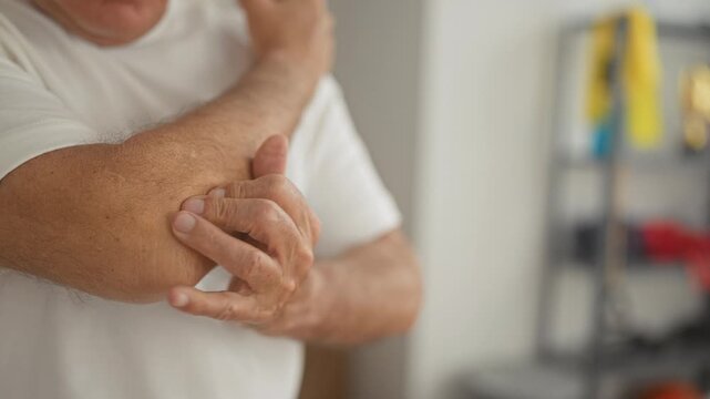 Man, middle age, holds elbow with hand in studio after training session for elbow pain and tenderness; concern recovery.
