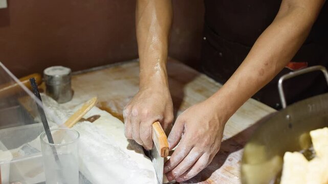 Asian Chef Using Bench Scraper to Cut Dough on Floury Surface