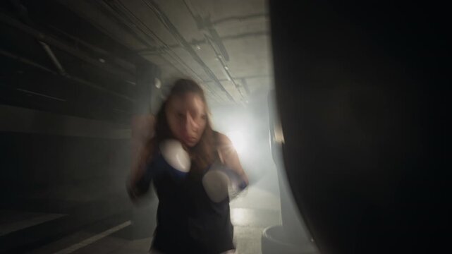 Young Caucasian woman punching heavy bag during intense workout in boxing gym. Footage is ideal for fitness brand commercials and motivational sports videos