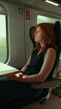 A red-haired woman looks out the window of a train while traveling home