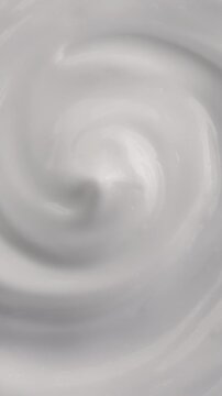 White Cream Swirling. Thick glossy cream moves in smooth folds, creating a soft abstract cosmetic texture.	