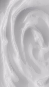 White Cream Swirling. Thick glossy cream moves in smooth folds, creating a soft abstract cosmetic texture.	