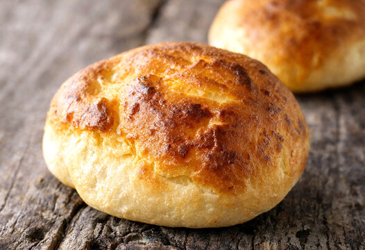 Freshly baked golden brown crusty bread rolls on rustic wooden table closeup view