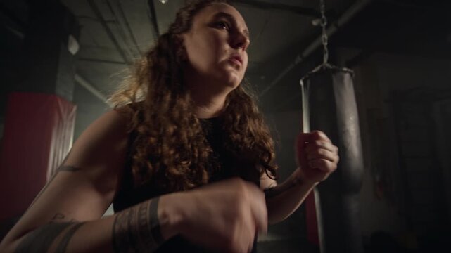 Young Caucasian woman with tattoos warming up wrists and shadowboxing in gym. Footage is perfect for fitness brand advertisements, motivational campaigns, and female empowerment promos