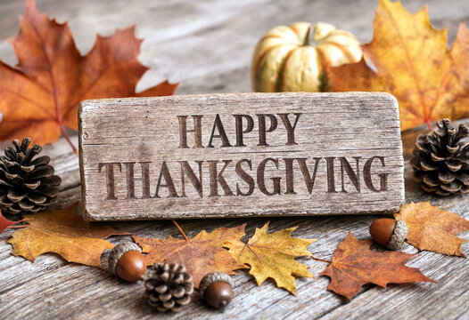 Happy thanksgiving wooden sign surrounded by autumn leaves pumpkins and pinecones on rustic table