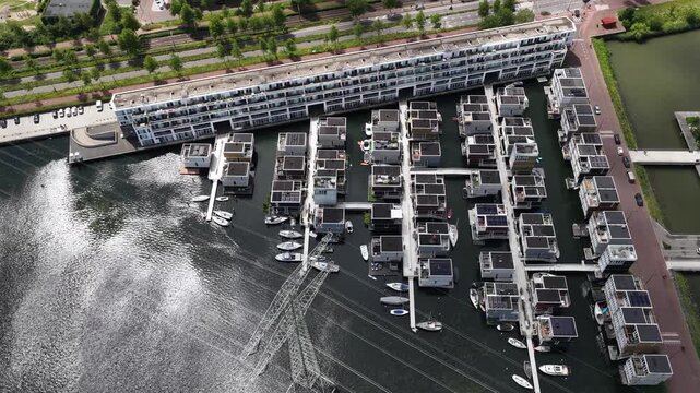 Top down aerial view slowly rotating over modern sustainable floating houses with solar panels on the roof, a unique architectural solution for waterside living in a marina in the netherlands